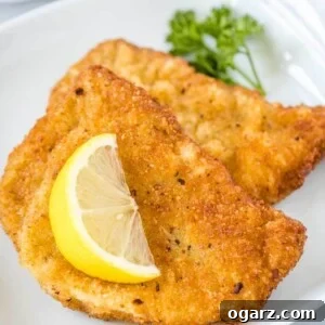 Two fried Schnitzels on a white plate, garnished with a wedge of lemon and parsley