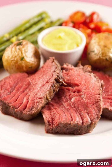 Magnificent Châteaubriand steak served medium-rare, accompanied by classic Sauce Béarnaise, tender roasted baby potatoes, crisp roasted asparagus, and vibrant cherry tomatoes.
