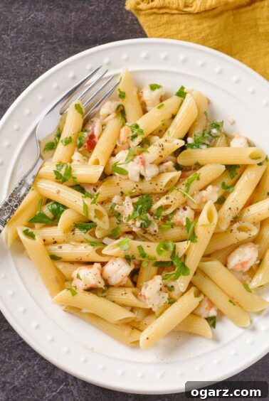 Luxurious Lobster tail pasta with penne, tossed in a fragrant shallot butter and white wine sauce, served on a pristine white plate and elegantly garnished with fresh parsley.