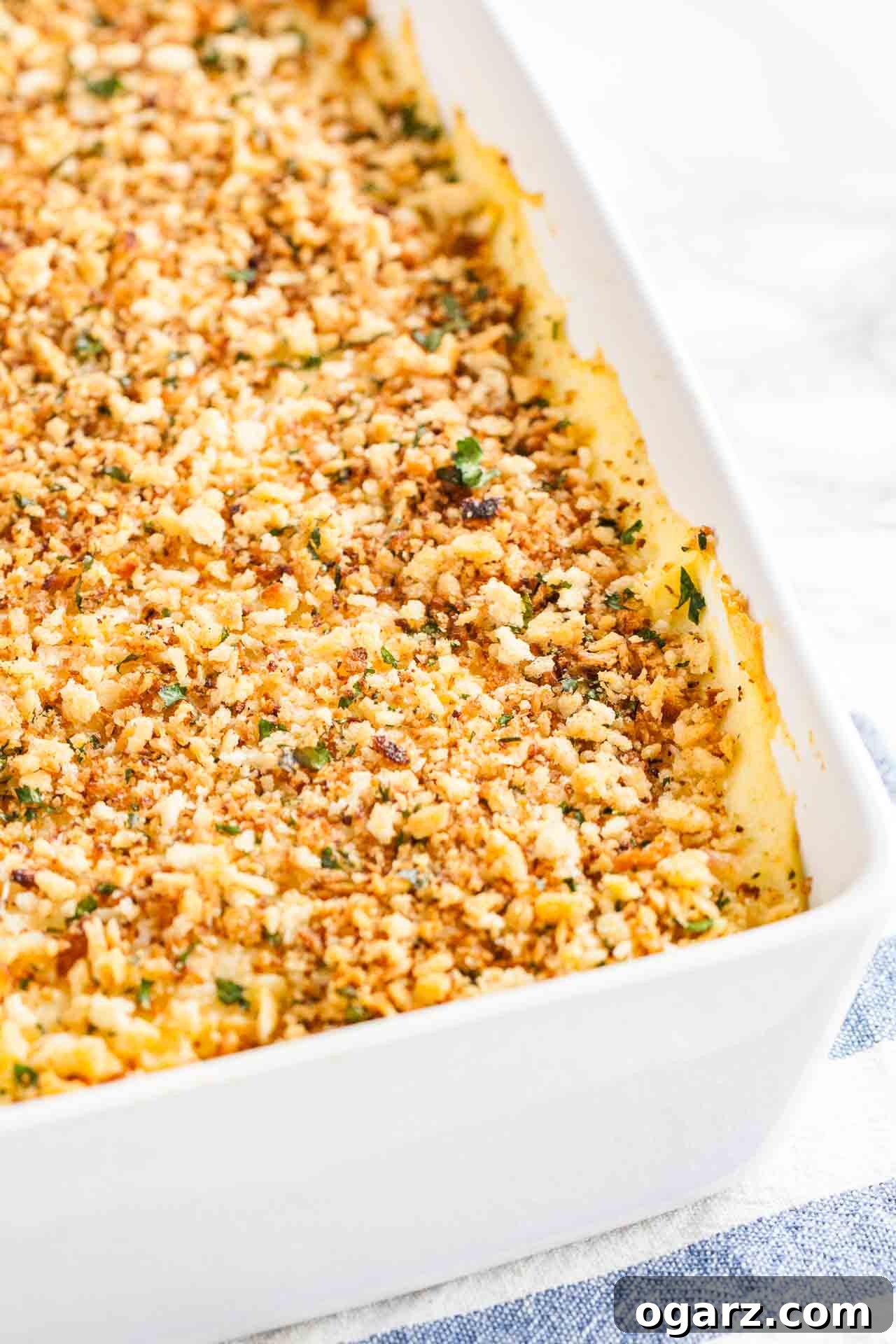 Tangy Kraut and Creamy Potato Bake 3 Close-up shot of a white rectangular baking dish filled with Sauerkraut Mashed Potato Casserole, resting on a blue and white patterned kitchen towel, ready to be served.