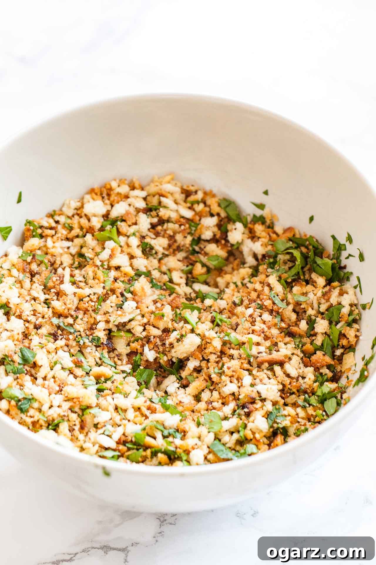 Tangy Kraut and Creamy Potato Bake 6 A pristine white bowl filled with golden toasted panko breadcrumbs mixed with vibrant green fresh parsley, ready to be used as a topping for the casserole.