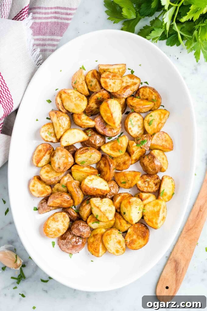 Crispy Air Fryer Potatoes 2 Perfectly crispy Air Fryer Roasted Potatoes on a white serving platter, garnished with fresh herbs.
