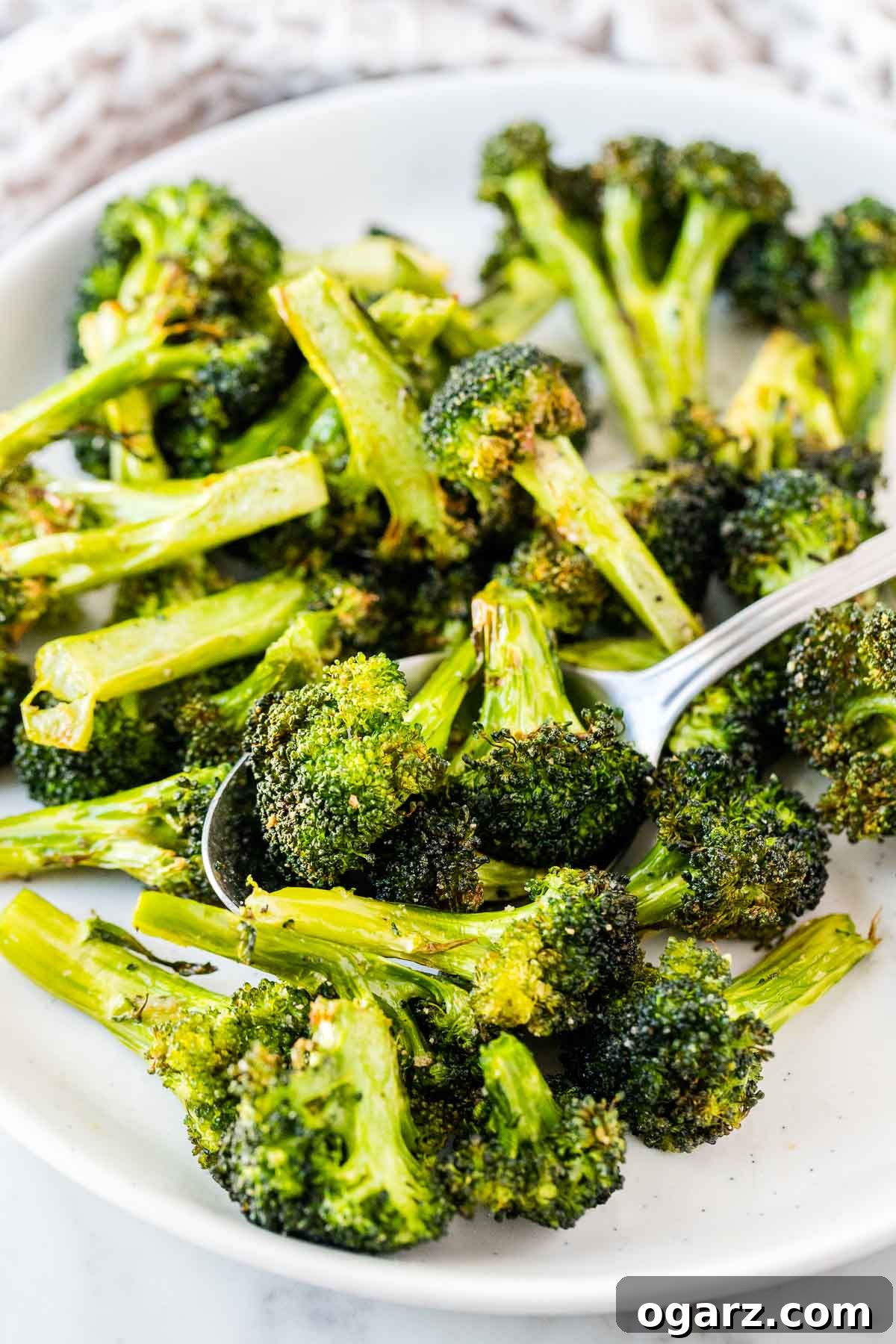 Crispy Air-Fried Broccoli 4 Broccoli florets on a white plate with a serving spoon, garnished with lemon.
