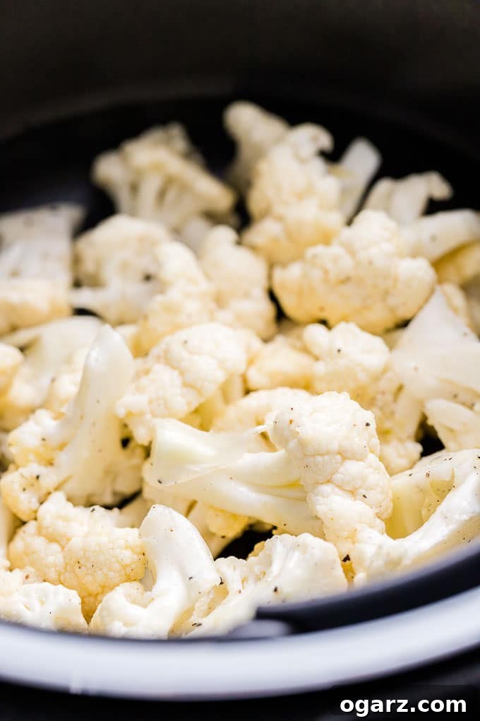 Perfectly Crispy Air Fryer Cauliflower 3 Raw cauliflower florets seasoned and ready in an air fryer basket.