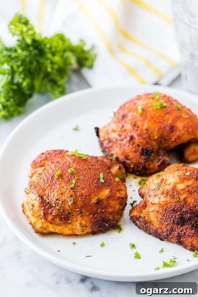 A close-up shot of perfectly golden-brown and crispy air-fried chicken thighs, garnished with fresh parsley on a rustic white plate, ready to be served.