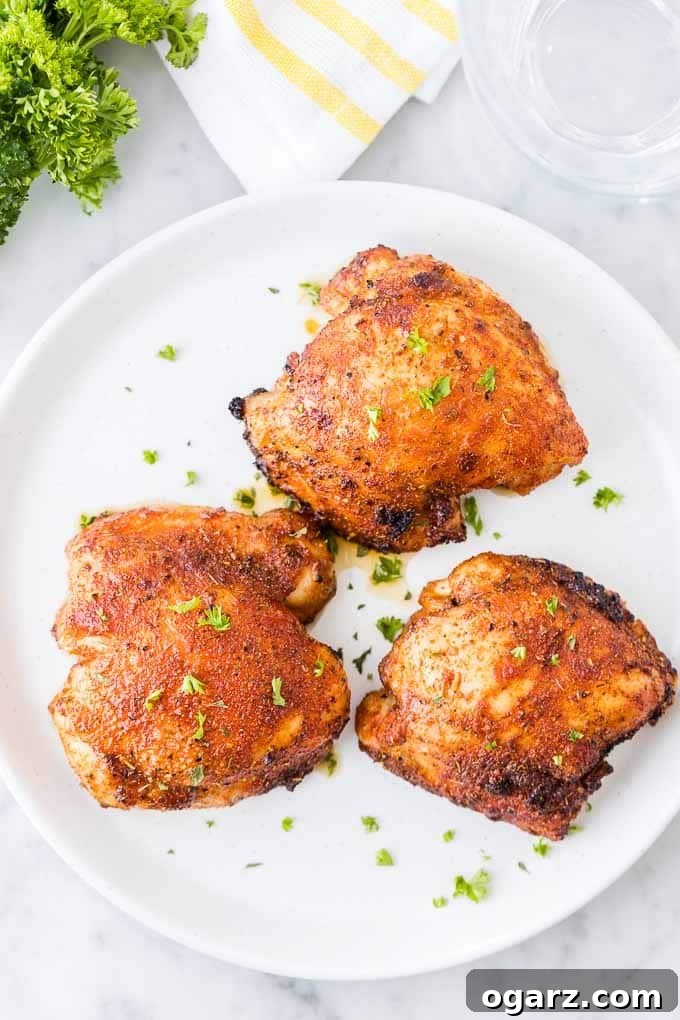 A serving of roasted chicken thighs, beautifully golden and garnished with fresh green parsley, presented on a simple white plate, ready to be enjoyed as a gourmet meal.