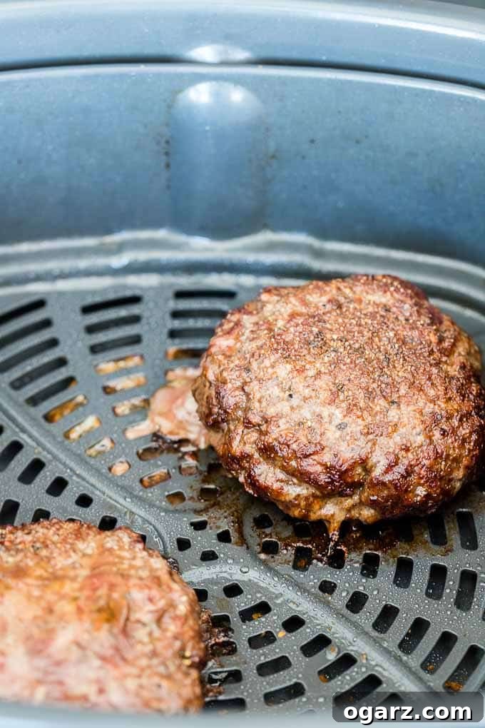 Two cooked hamburger patties in the Air Fryer basket with melted cheese