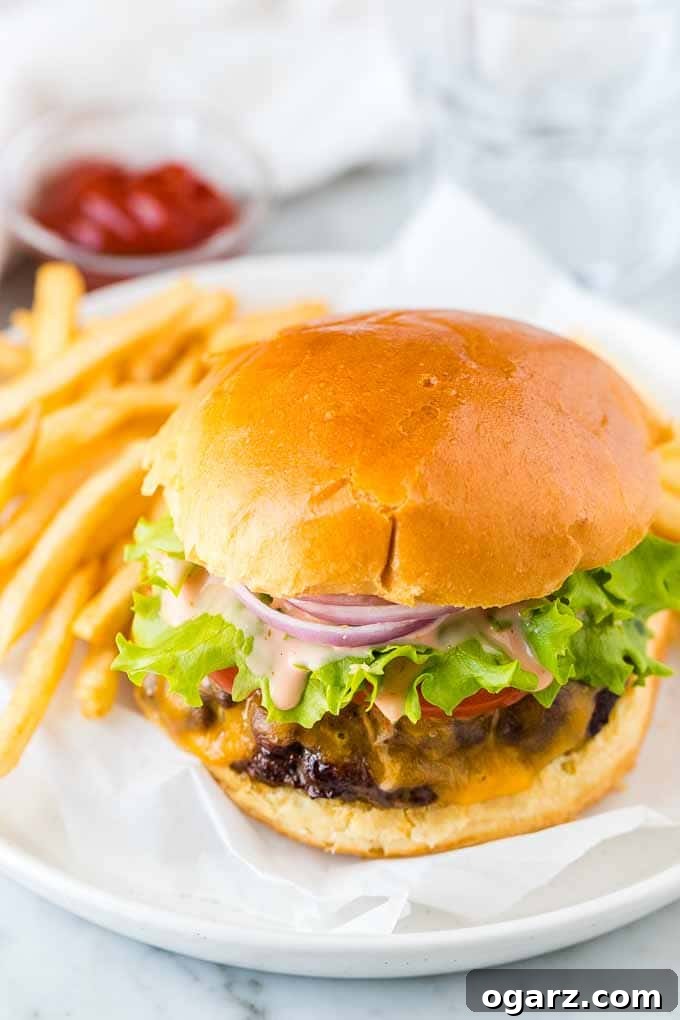 A perfectly assembled hamburger on a plate with crispy fries on the side