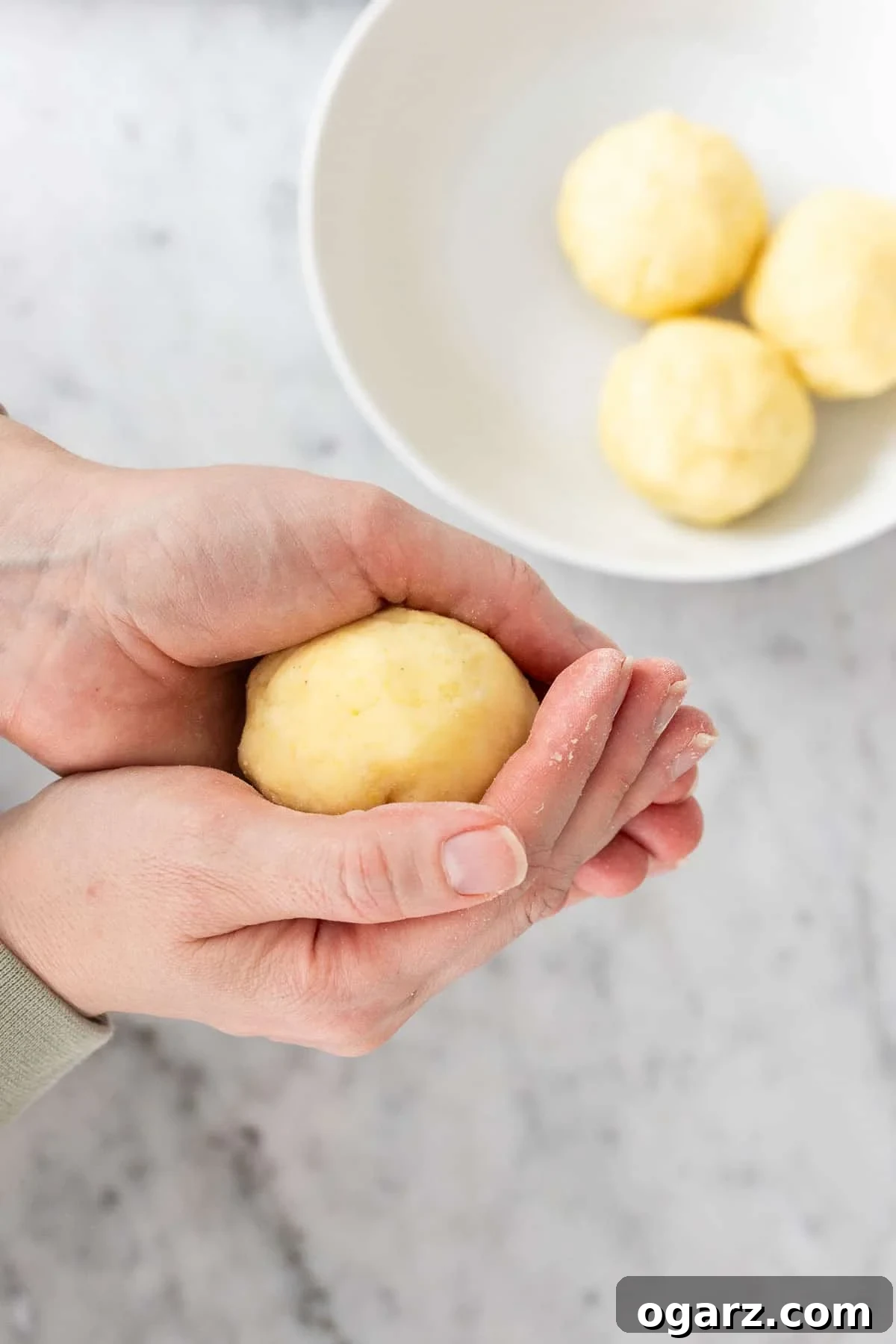 Pillowy Potato Bites 11 Hands carefully shaping a portion of potato dough into a perfectly round ball, preparing it for cooking.