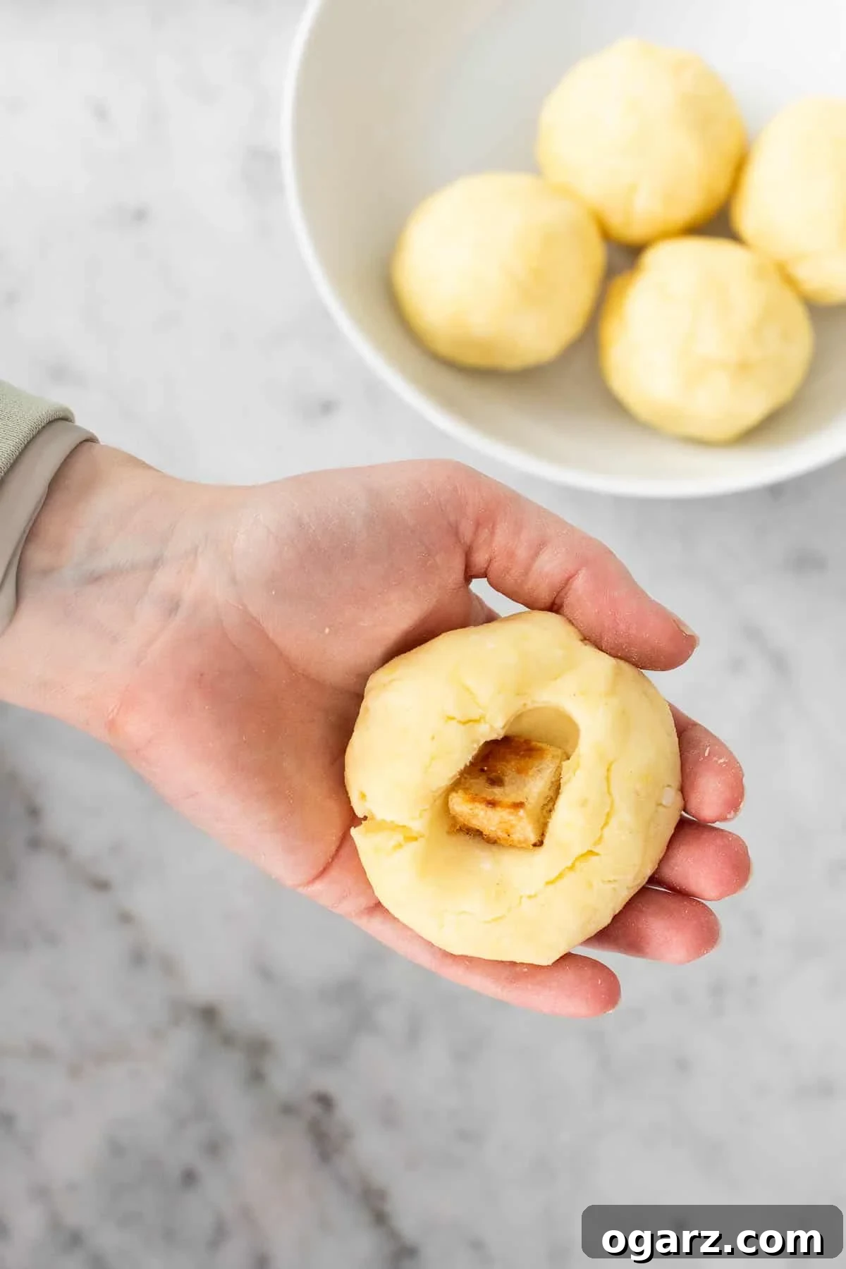 Pillowy Potato Bites 12 A bread cube being placed into the flattened center of a potato dough ball, ready to be sealed within.