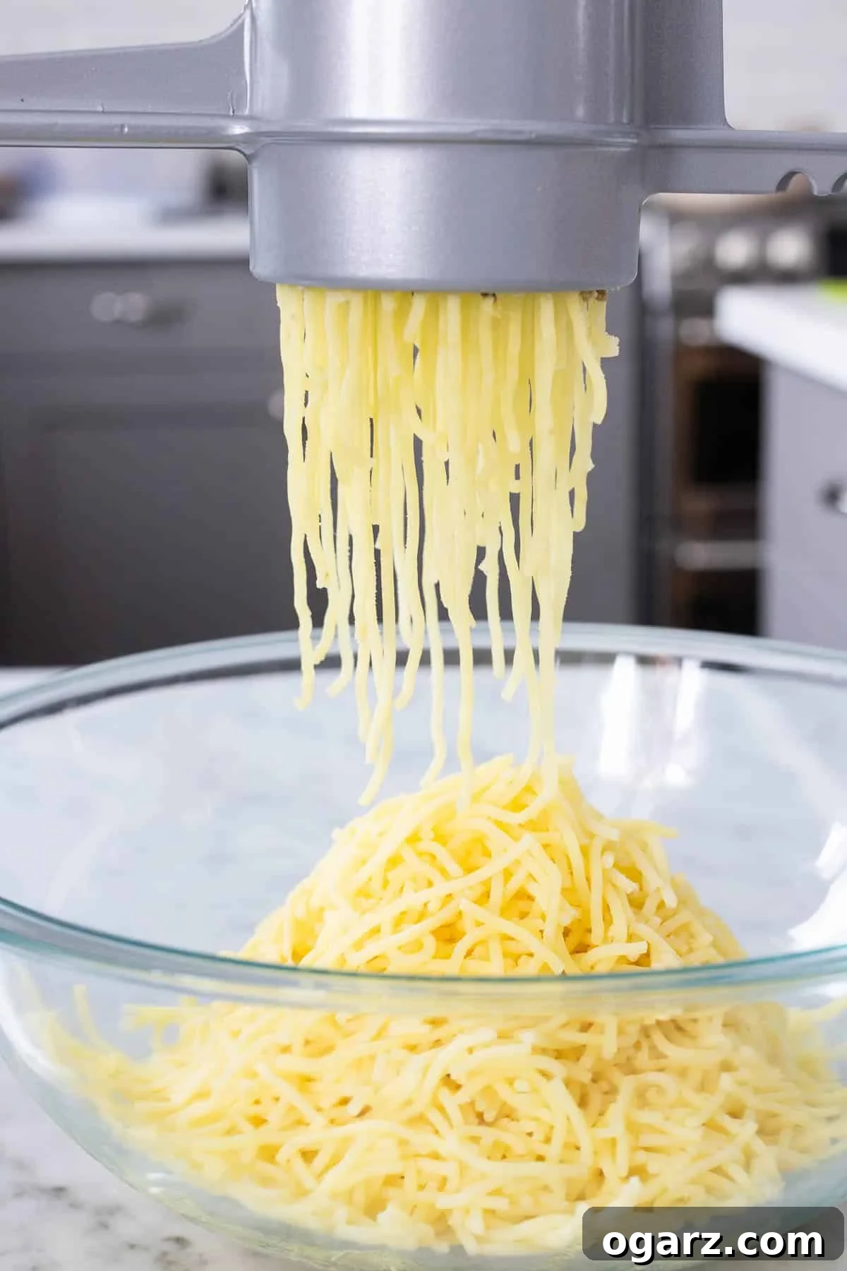 Pillowy Potato Bites 7 Hot, cooked potatoes being pressed through a potato ricer into a large bowl, creating fluffy strands.