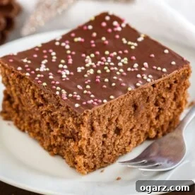 A white plate with a square of chocolate topped spice cake with a fork.