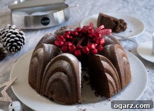 A white plate with german mulled wine cake, garnished with red jingle bells. A piece has been cut out and is lying on a white plate in the background next to an Alessi sugar bowl.