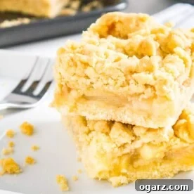 Two pieces of apple streusel cake stacked on top of each other on parchment paper with a fork next to it and a baking sheet in the background