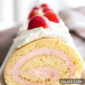 Close-up of a strawberry swiss cake roll topped with whipped cream and strawberries on a rectangular serving platter.