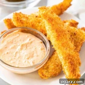 A heap of air fryer dill pickles on a white plate with a small glass bowl with a dip in it.