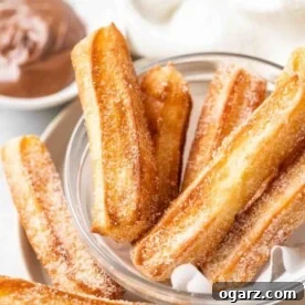 sugared churros in a glass bowl with parchment with a small white bowl of nutella in the background