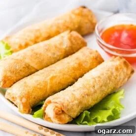 Egg Rolls on a white plate next to a bowl of sauce