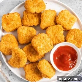 Chicken nuggets on a white plate with a small bowl of ketchup.