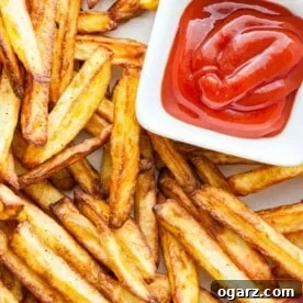 Top-down shot of brown, crispy fries with a small, white, rectangular bowl of ketchup.