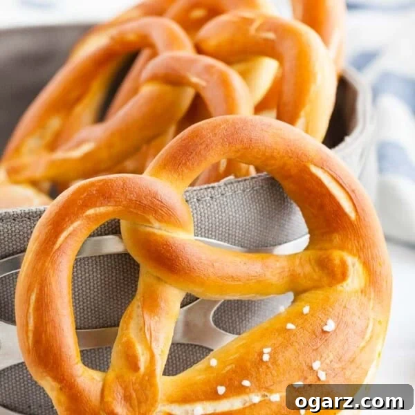 A pretzel leaning against a bread basket, containing more pretzels with a white and blue dish towel in the background.