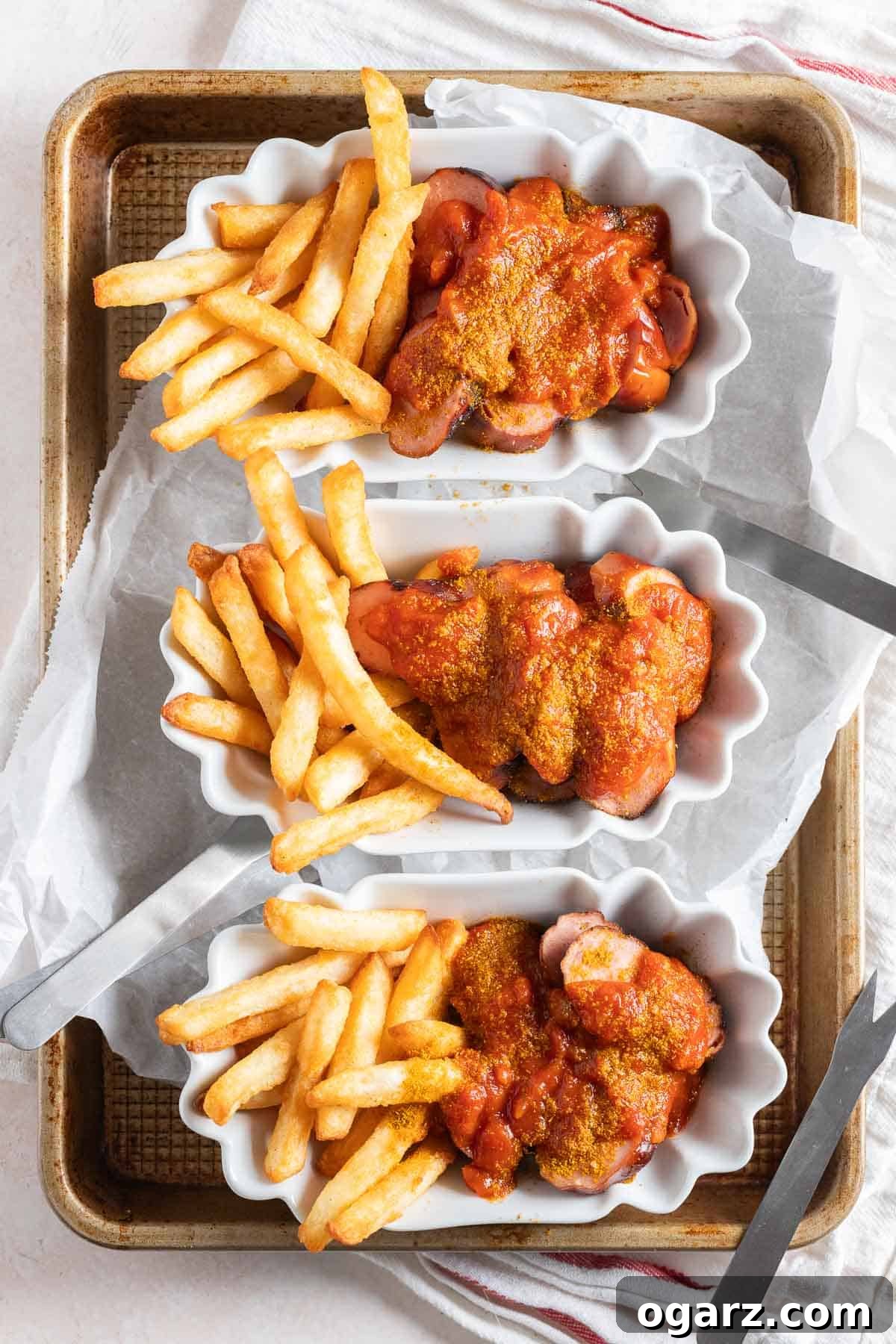 Three white serving dishes filled with currywurst and fries.