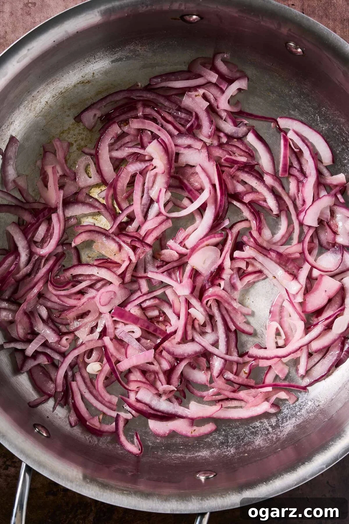 Caramelized Apples and Onions for Roasts and Salads 4 Sliced red onions sautéing in a stainless steel skillet, beginning to soften and turn translucent.